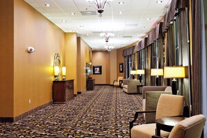 Un pasillo de hotel con alfombra estampada, zonas de estar y un candelabro.
