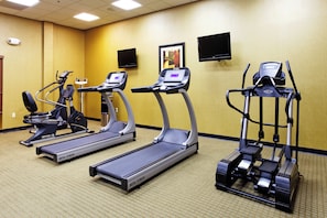 Un gimnasio con tres cintas de correr, una bicicleta estática y una máquina de remo.