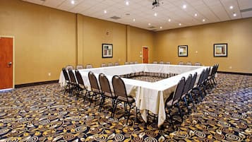 Ein Konferenzraum mit einem langen Tisch, umgeben von Stühlen, einem gemusterten Teppich und gerahmten Bildern an den Wänden.