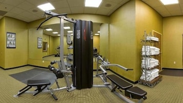 Un gimnasio con equipamiento de ejercicio, una banca y un estante con toallas.