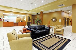 A hotel lobby with a reception desk, a black leather sofa, a beige armchair, a patterned rug, and a decorative wall piece. - Holiday Inn Batesville by IHG (Batesville)