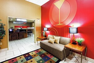Un interior moderno con una pared roja de acento, un sofá estampado, una mesita con una lámpara y una zona de cocina al fondo.