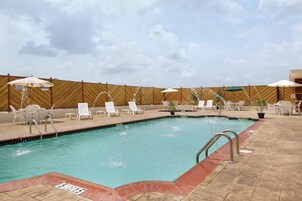 Una piscina con sillas de descanso y sombrillas, rodeada por una cerca de madera.