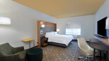 A hotel room with a bed, a desk, a chair, a small table, and a TV.