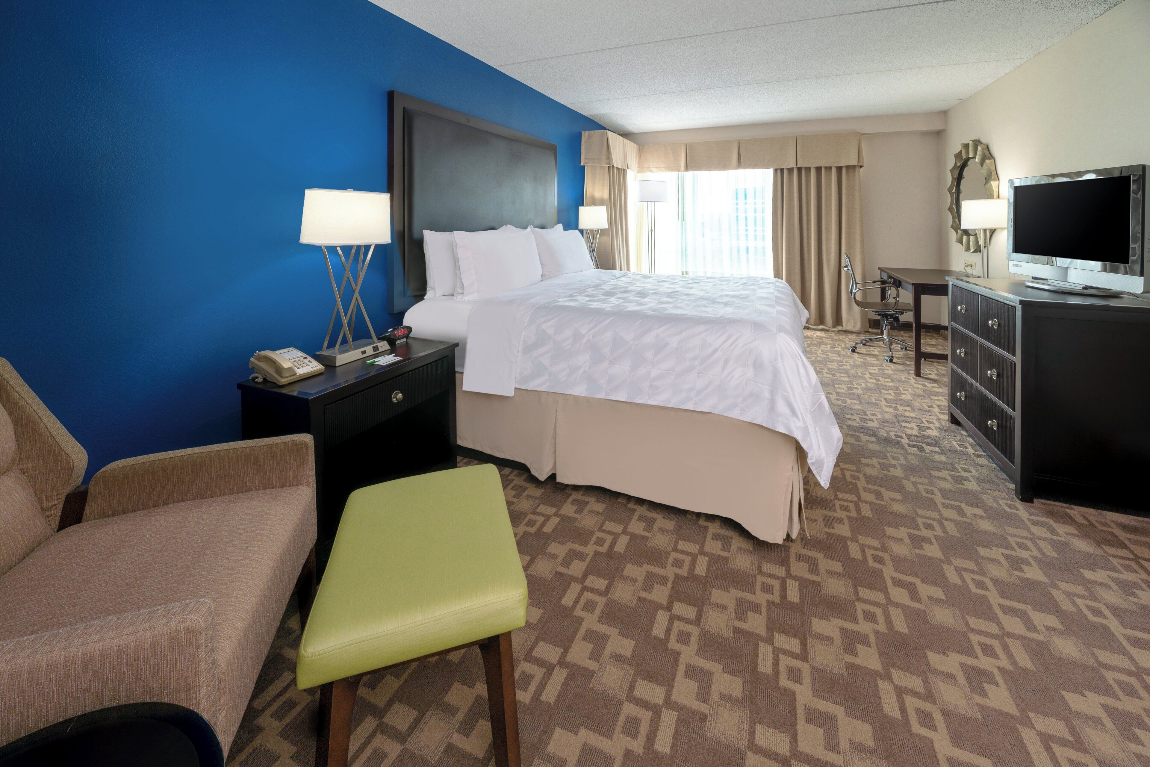 A hotel room with a bed, a desk, a chair, a TV, and a phone on the nightstand.