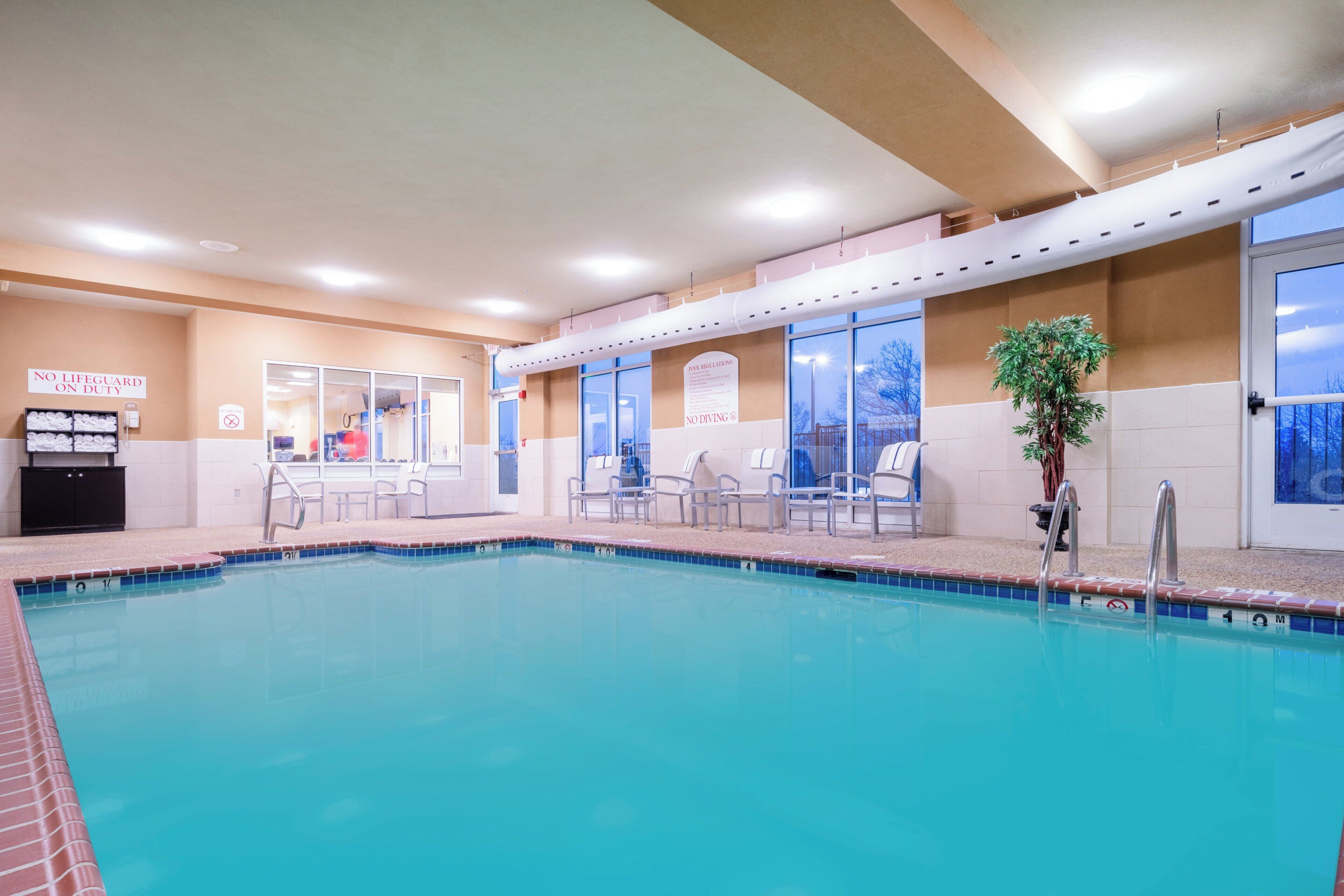 An indoor swimming pool with clear poolside chairs, a lifeguard station, and a sign indicating no diving.