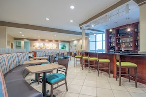 A restaurant with booths and tables, a bar area with shelves of bottles, and a large window providing natural light. - Holiday Inn Manassas - Battlefield by IHG (Manassas)
