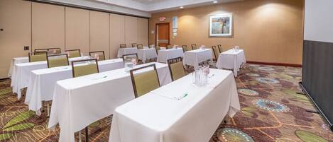 Un salón de conferencias con varias mesas, sillas y una pantalla para proyector.