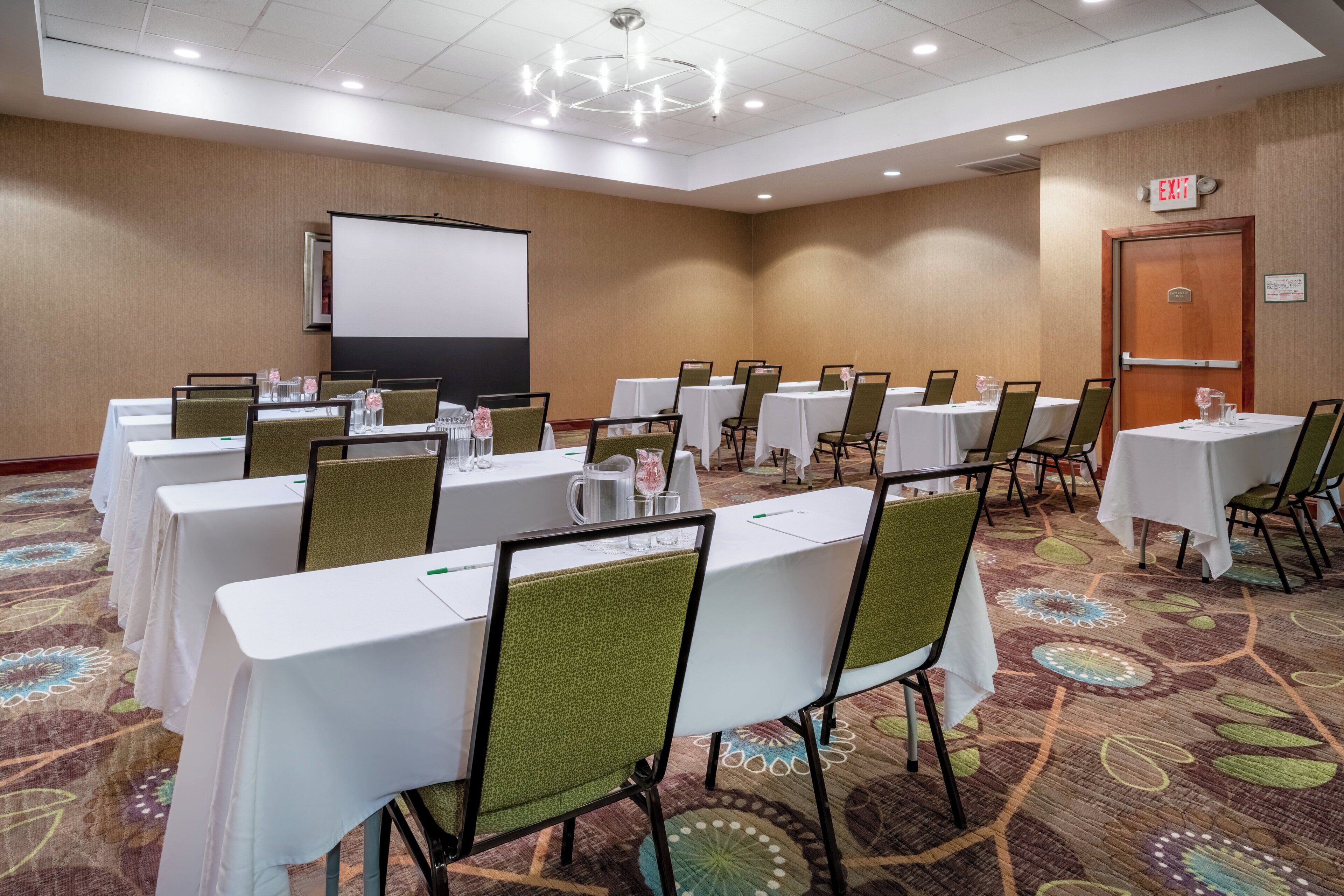 A conference room with tables and chairs, a projector screen, and an exit door.