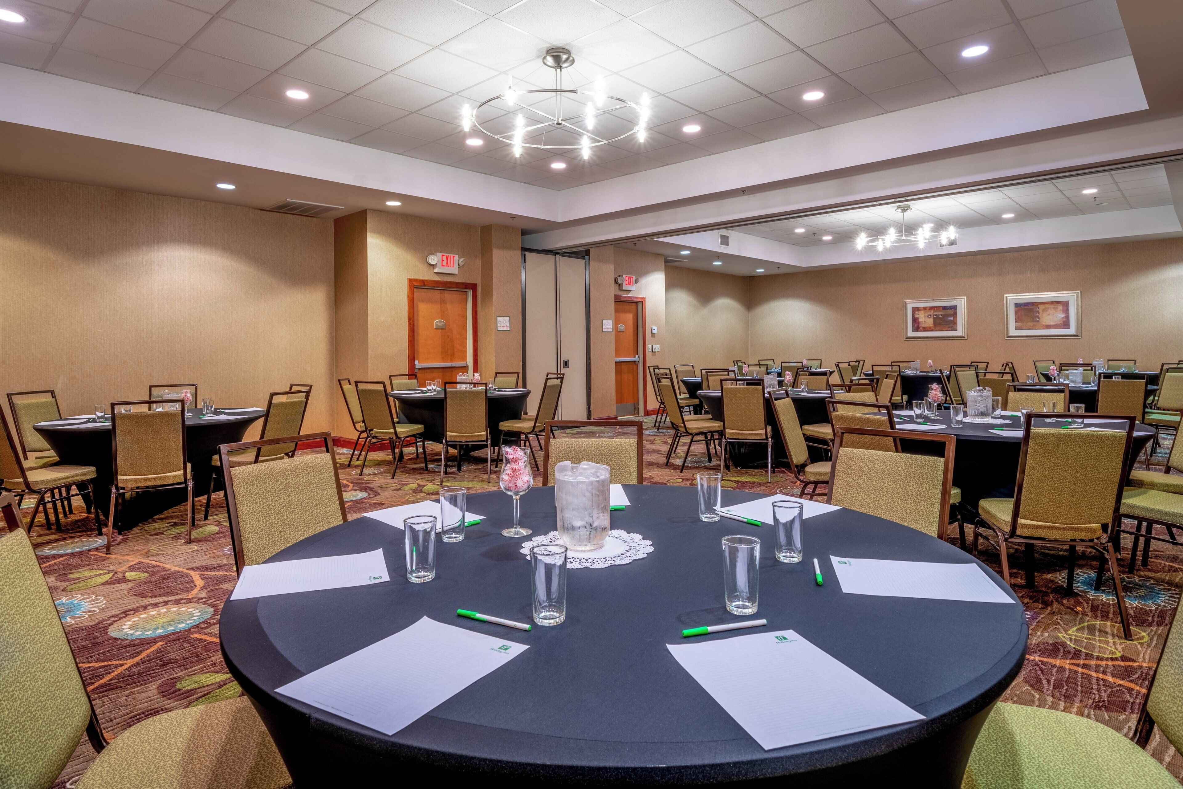 Une salle de conférence équipée de tables rondes, de chaises et d’un grand lustre.
