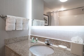 Een badkamer met een granieten blad, een wastafel, een spiegel en een handdoekrek met meerdere handdoeken.