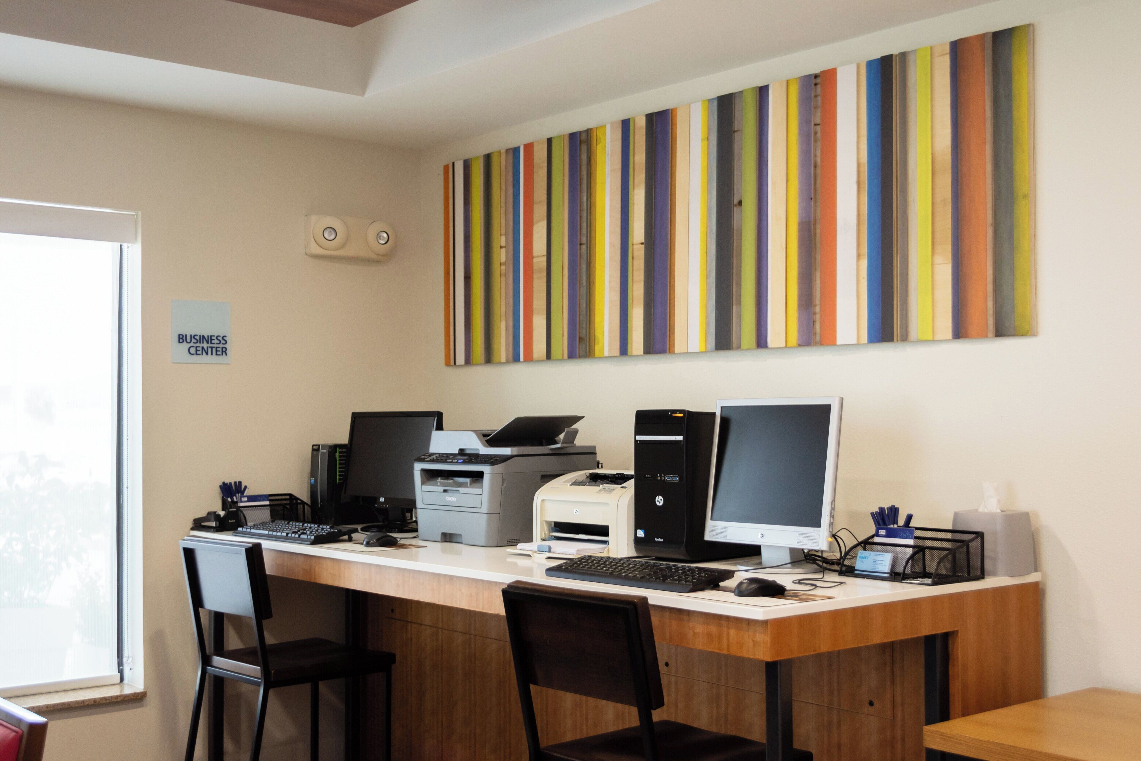 Un centro de negocios con un escritorio amplio, varias computadoras, impresoras y dos sillas.