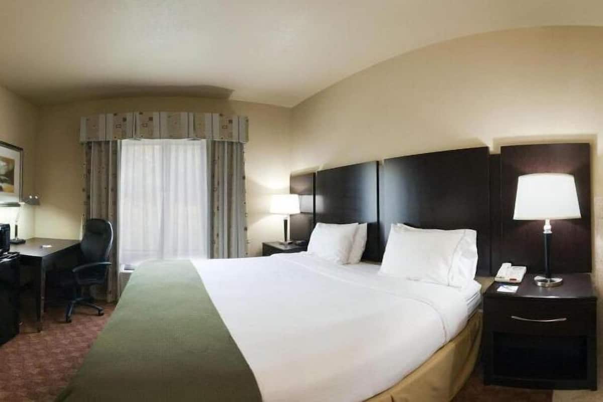 A hotel room with a large bed, a desk with a chair, a nightstand with a lamp, and a separate bathroom with a bathtub.