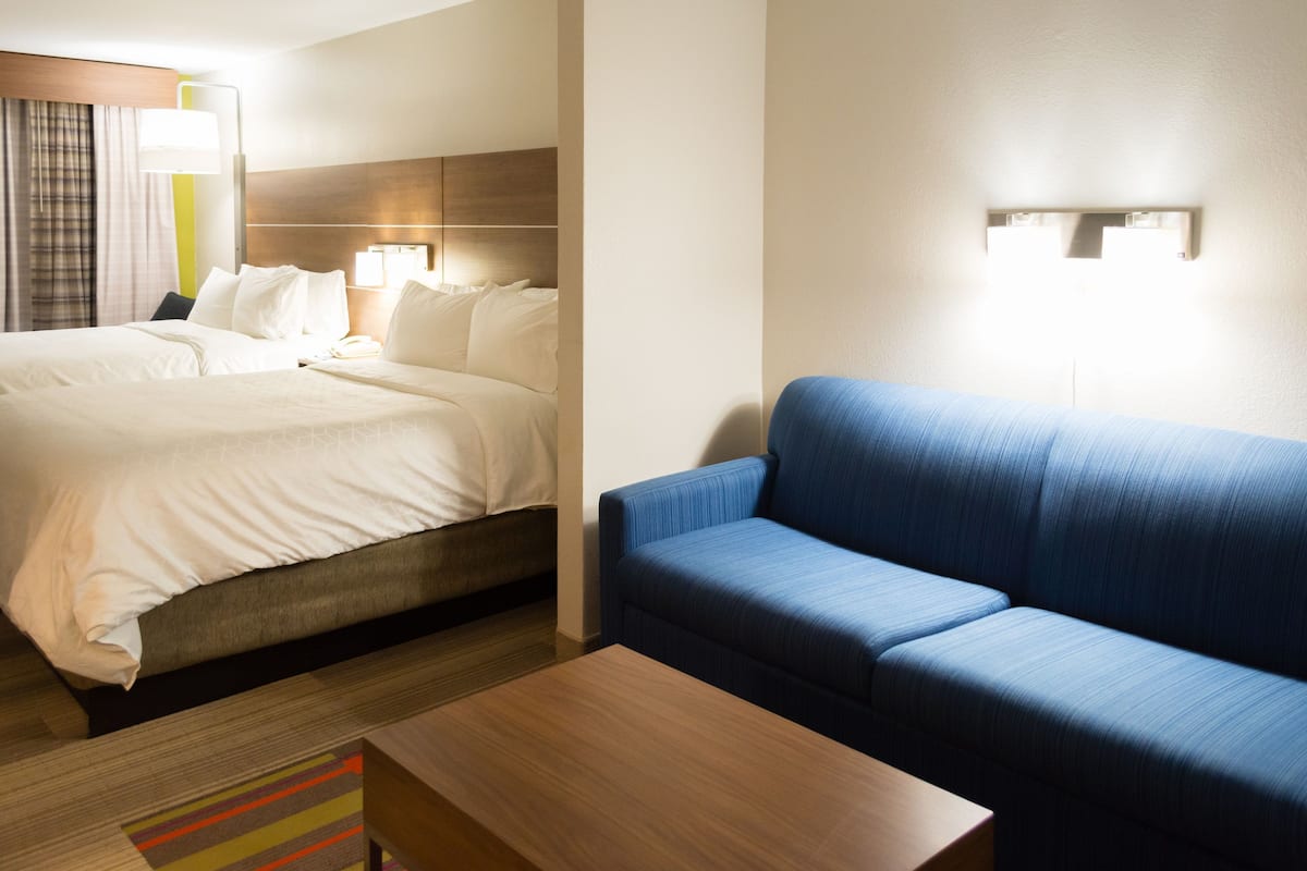 A hotel room with a bed, a blue sofa, a wooden coffee table, and a lamp.