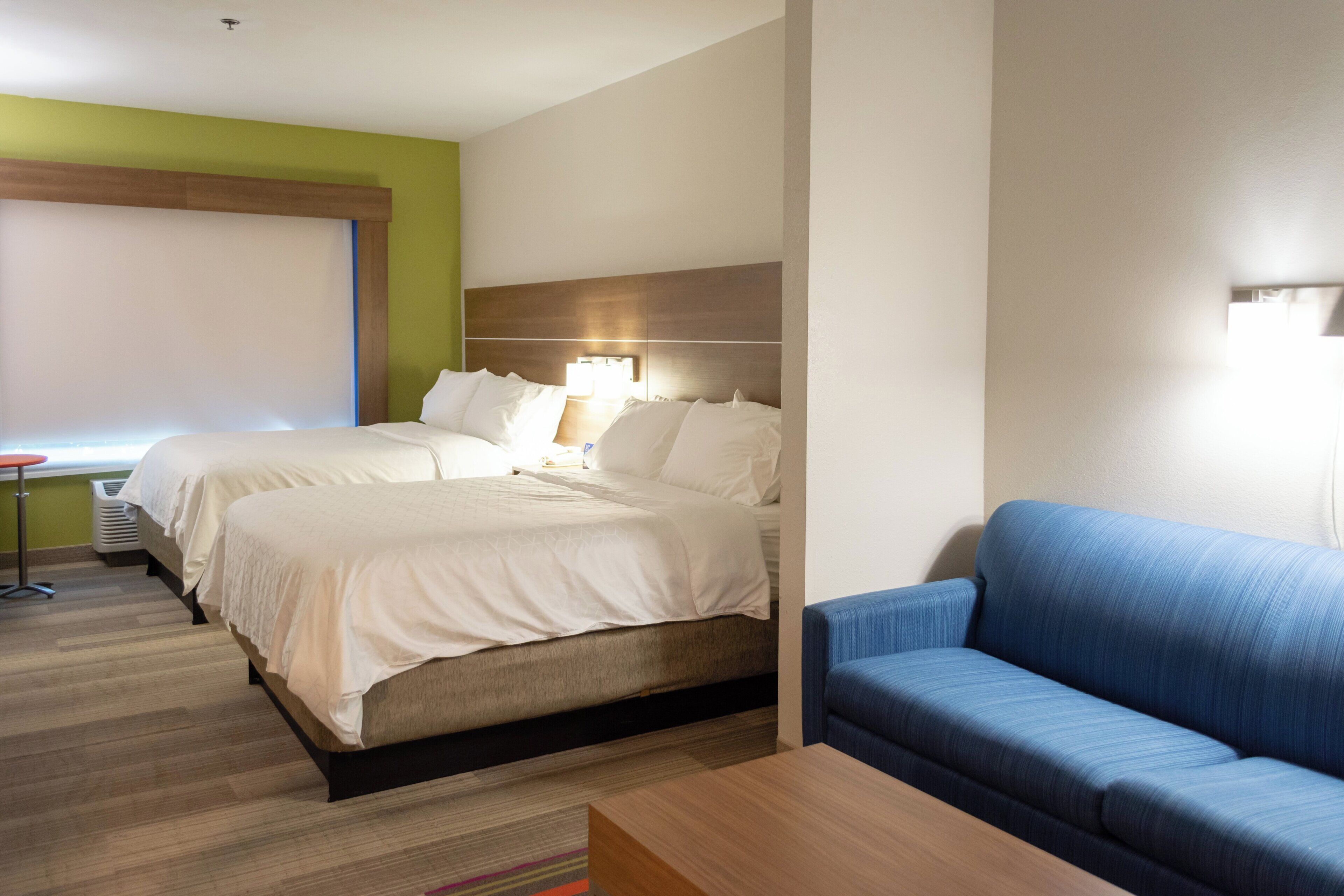 A hotel room with a bed, a blue sofa, and a desk with a lamp.