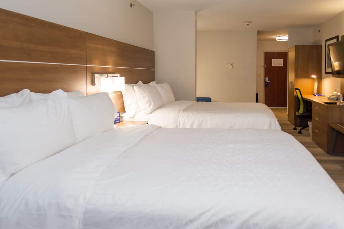 A hotel room with two beds, a desk, a chair, and a TV.