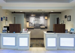 A hotel reception area with two reception desks, a central information board, and a patterned carpet.