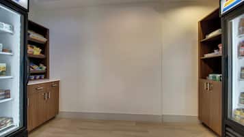 A room with two refrigerators stocked with snacks and beverages, wooden cabinets, and a tiled floor.