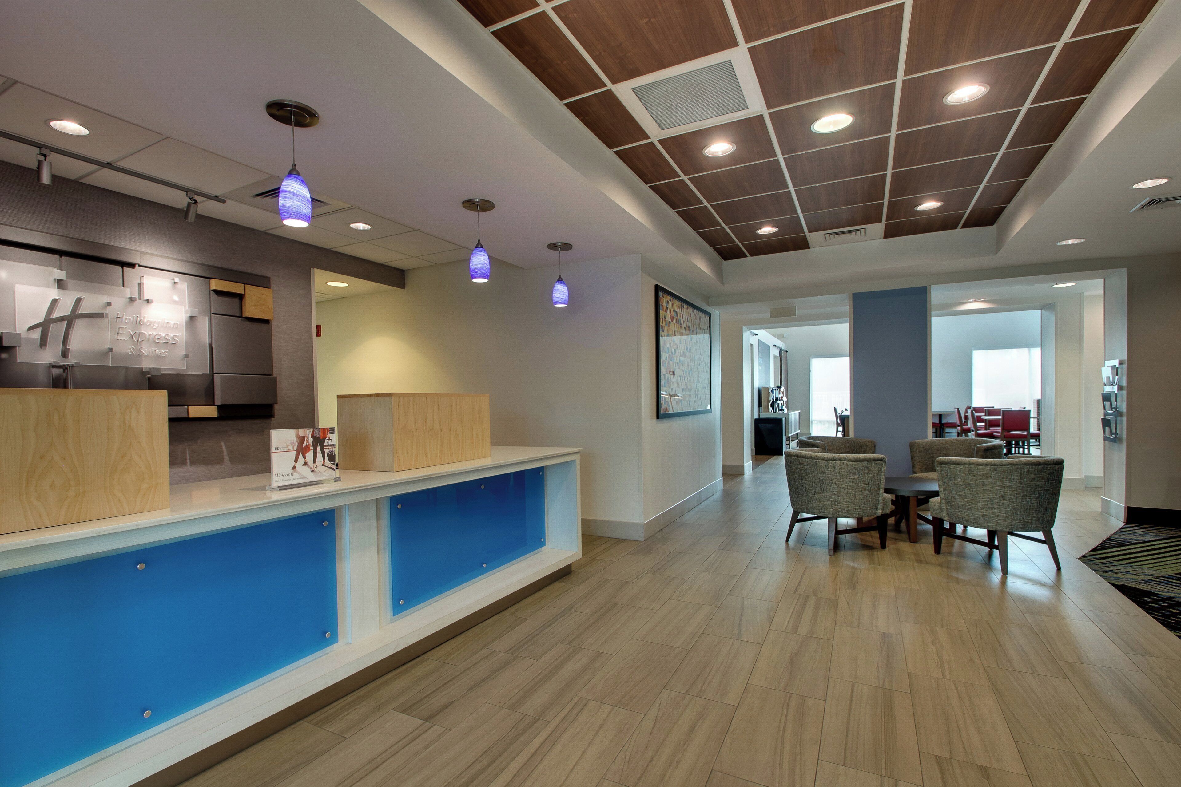 A hotel reception area with a wooden reception desk, blue accent wall, and a seating area with chairs and a table.