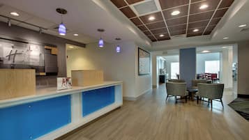 A hotel reception area with a wooden reception desk, blue accent wall, and a seating area with chairs and a table.