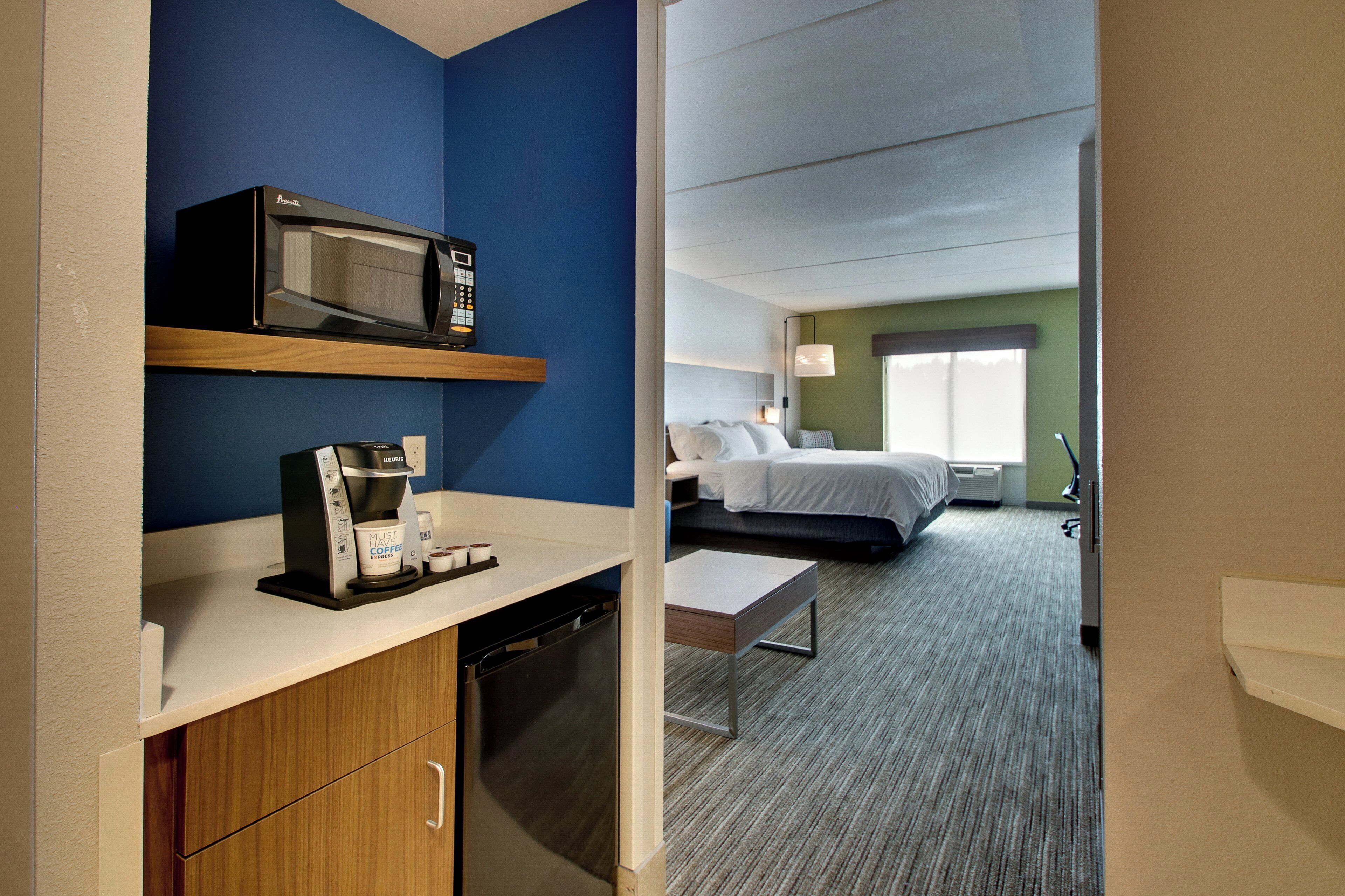 Quarto de hotel com cozinha compacta, uma cama, mesa de cabeceira e janela.