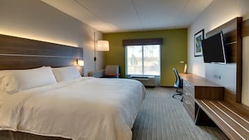 A hotel room with a large bed, a desk, a chair, a television, and a window with a view of trees.