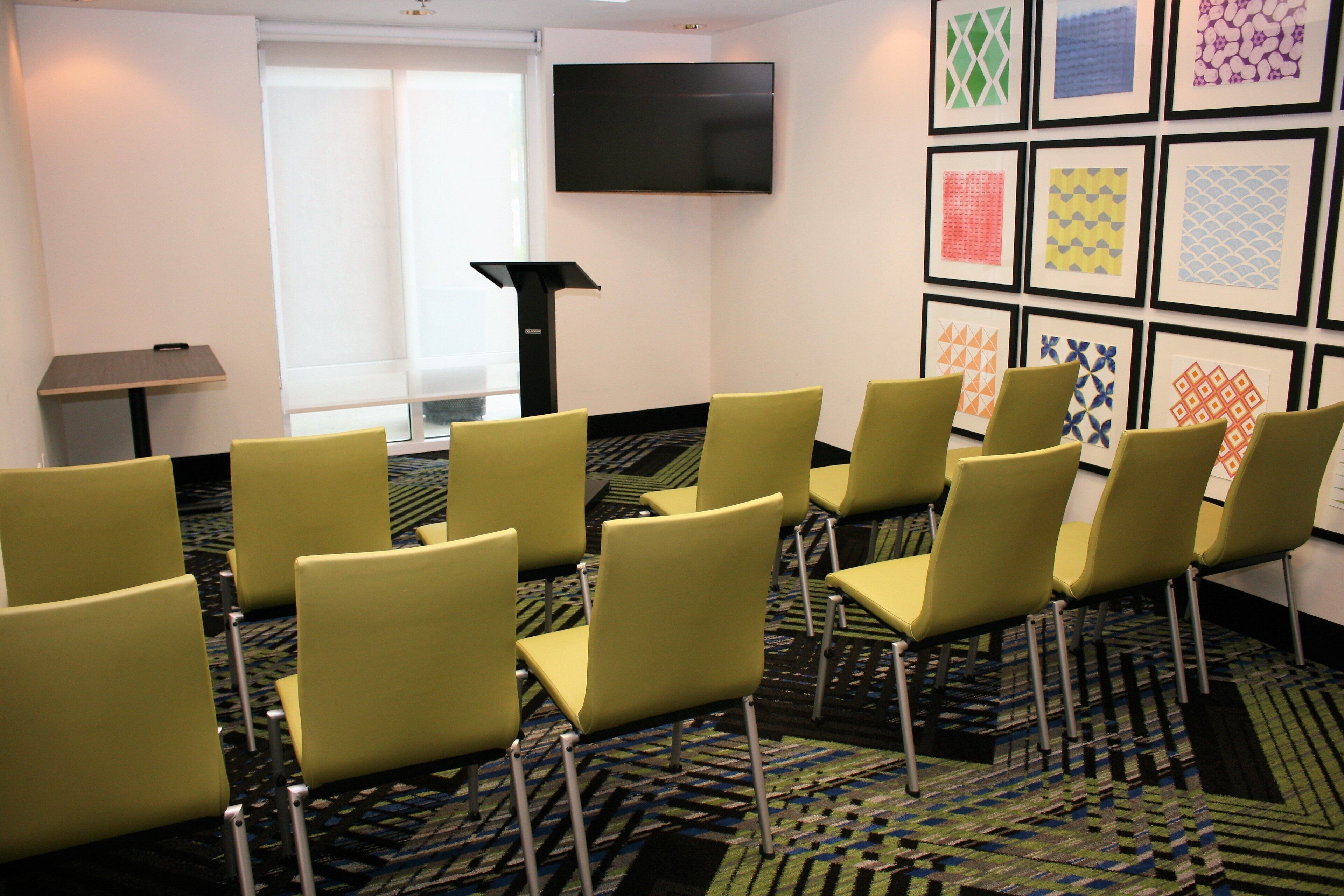 A conference room with yellow chairs, a flat-screen TV, and framed artwork on the wall.
