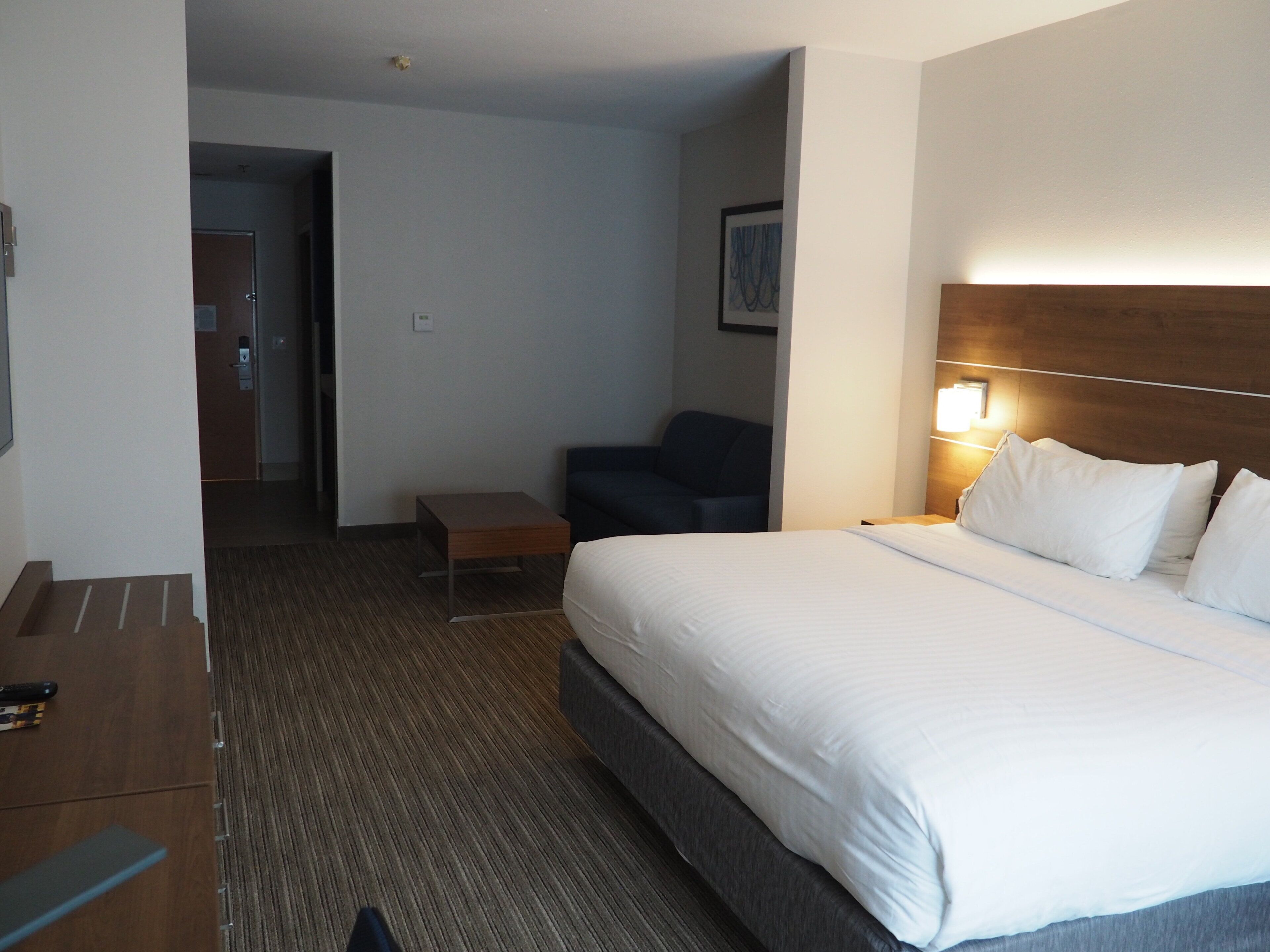 A hotel room with a bed, bedside table, chair, and a small table.