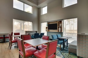 Una habitación de hotel moderna con zona de comedor, ventanas amplias y televisor de pantalla plana.