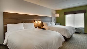 Ett hotellrum med två sängar, en sänggavel i trä, sänglampor, ett fönster med persienner och ett golv med heltäckningsmatta.