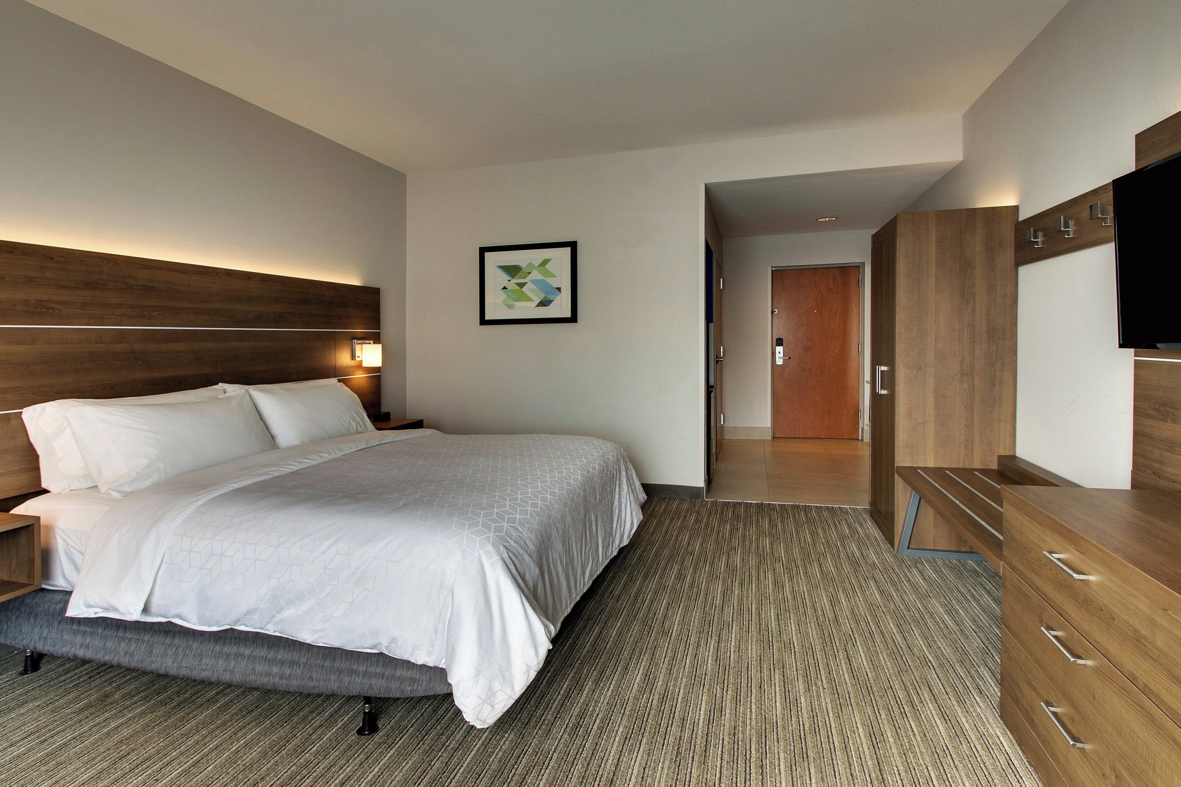 Une chambre d’hôtel avec un grand lit, une tête de lit en bois, un téléviseur à écran plat et une œuvre d’art encadrée accrochée au mur.