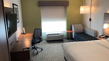 Ein Hotelzimmer mit einem Bett, einem Schreibtisch mit Stuhl, einem kleinen Tisch, einem Standheizkörper und einem Fenster mit Jalousien.