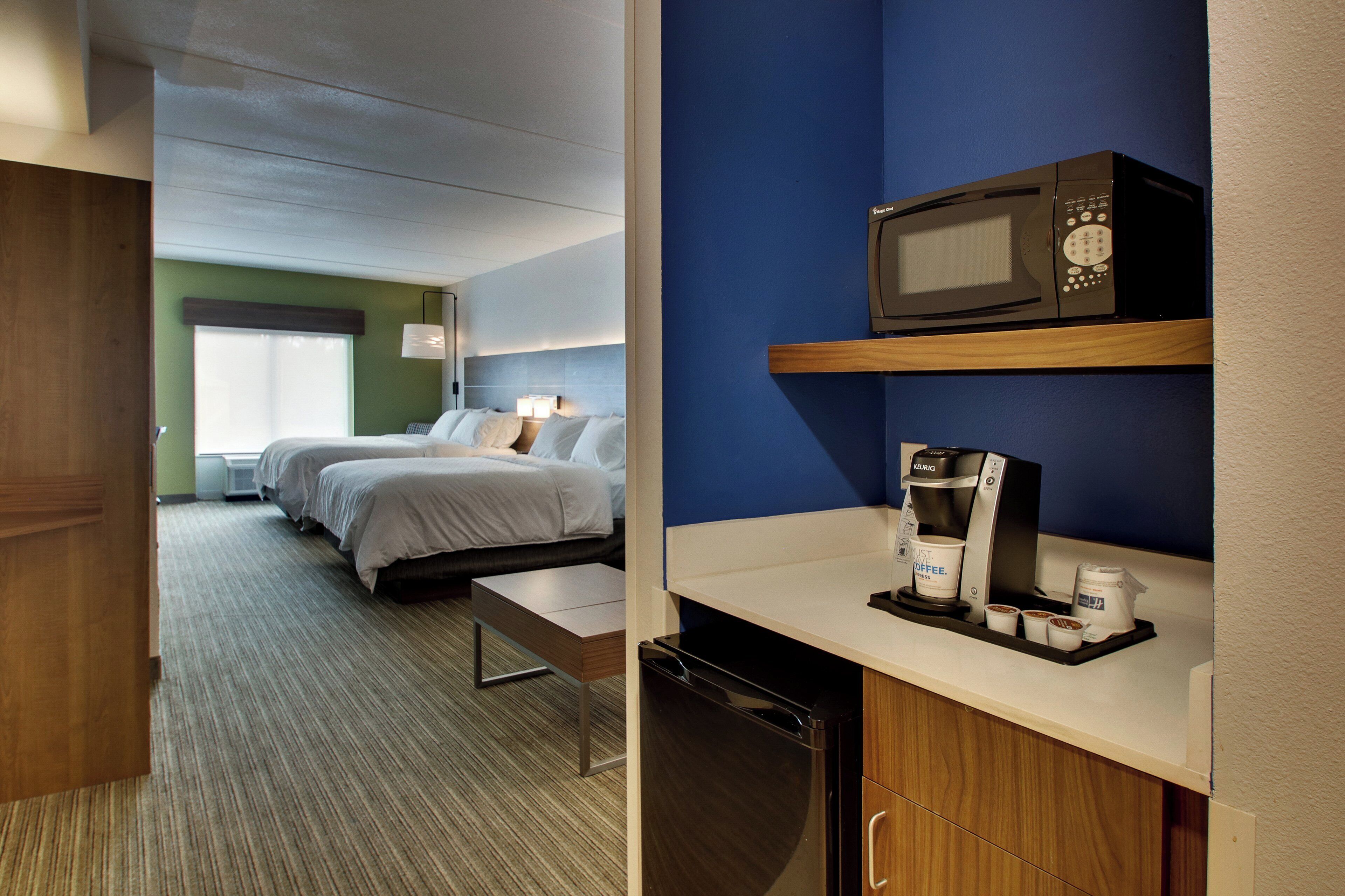 Habitación de hotel con dos camas, microondas, cafetera y una pequeña mesa.
