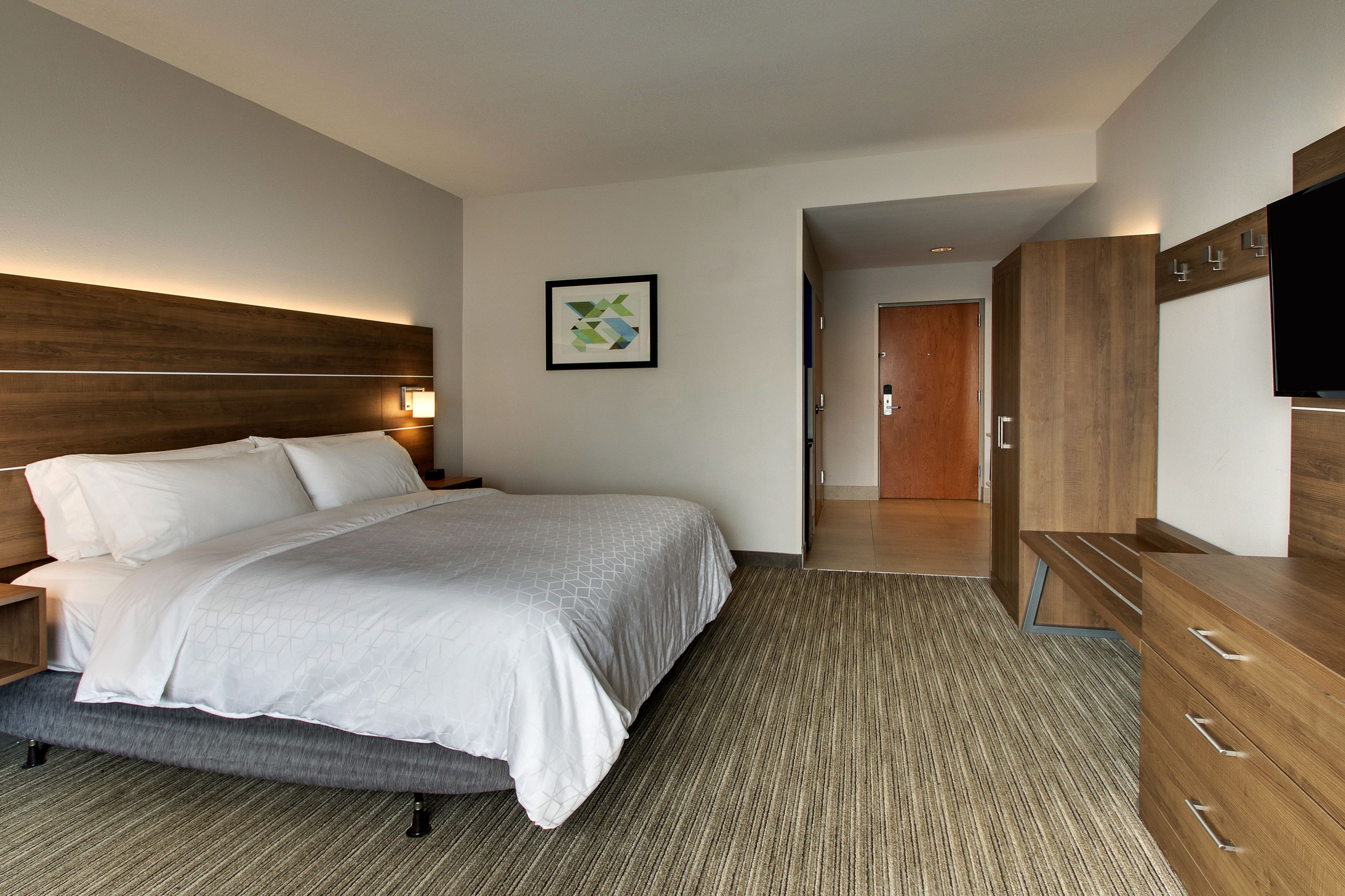 Una habitación de hotel moderna con una cama grande, cabecera de madera, televisor de pantalla plana y vestidor.