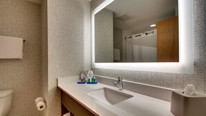 A modern bathroom with a large mirror, white sink, and a wooden vanity.