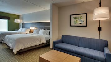 A hotel room with two beds, a sofa, a small table, and a wall-mounted lamp.
