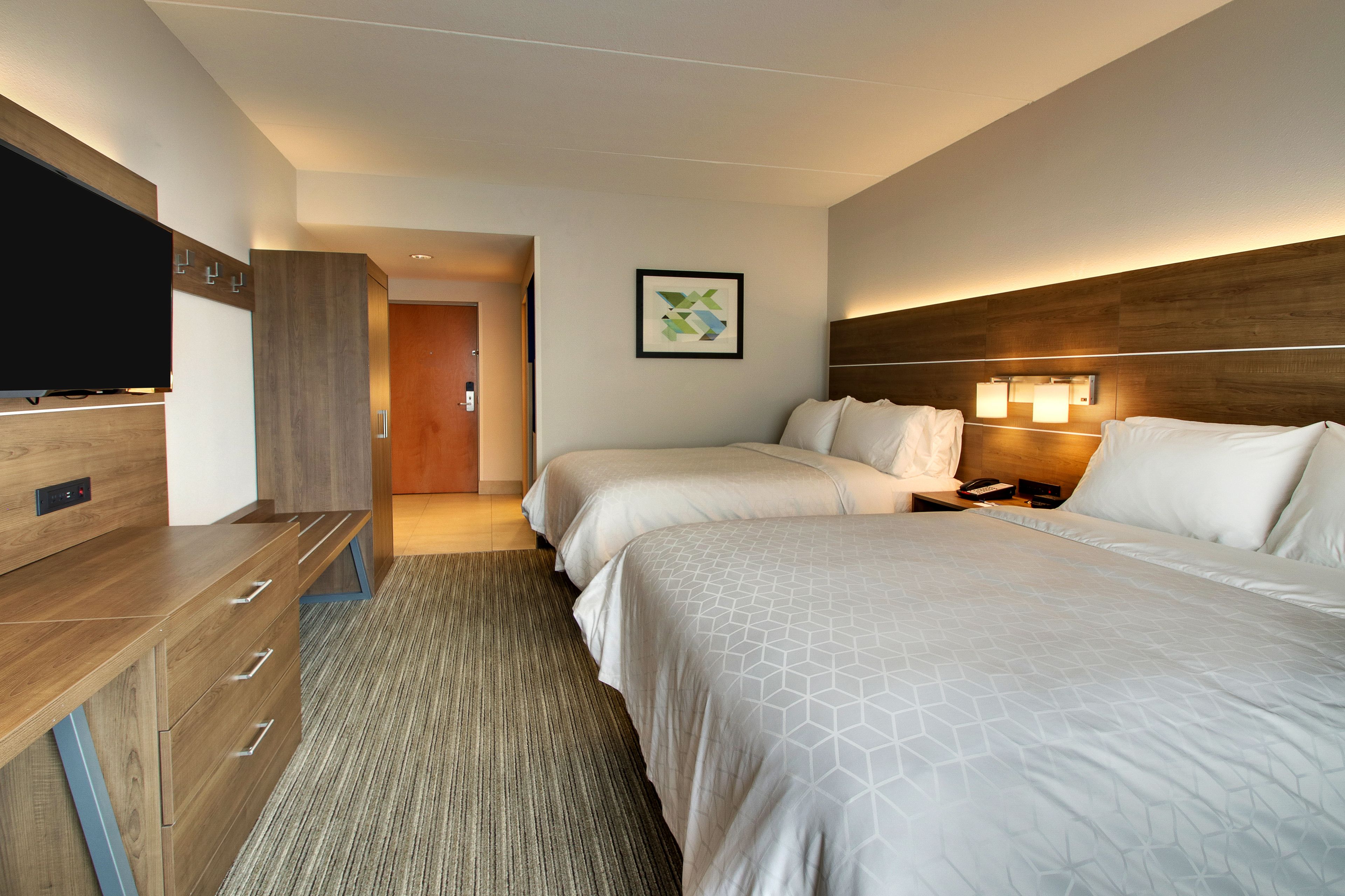 A hotel room with two beds, a TV, a wooden desk, and a framed picture on the wall.
