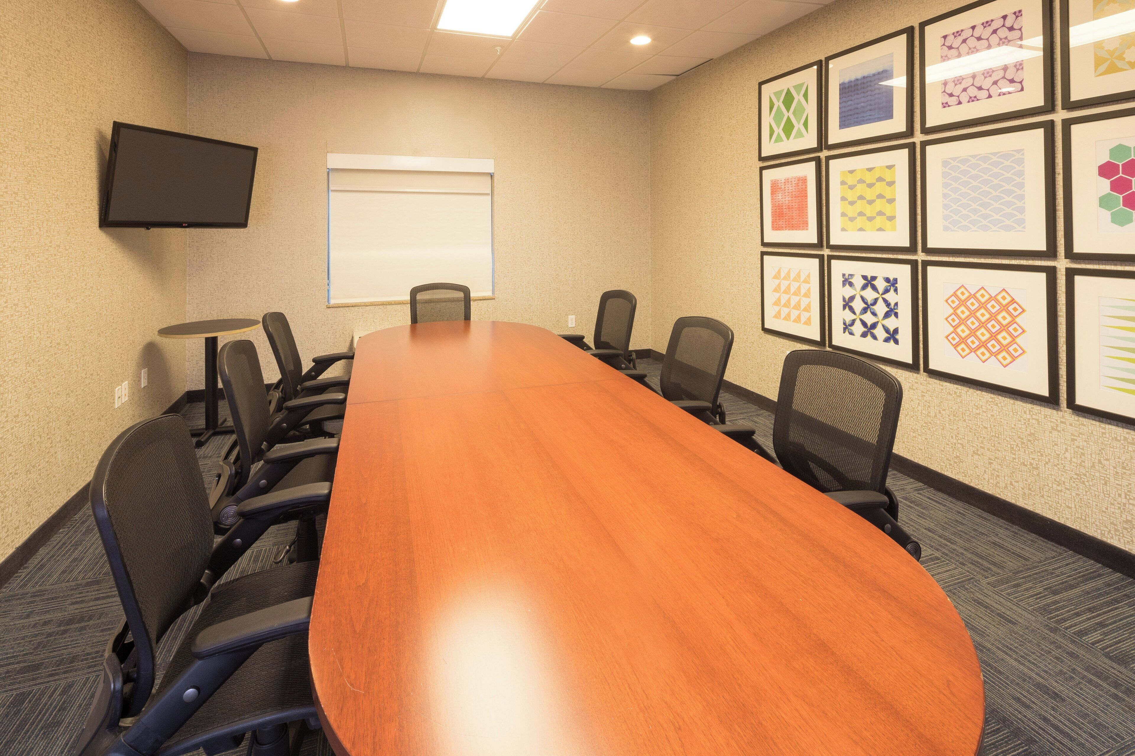 A conference room with a long table, chairs, a projector screen, and framed artwork on the walls.
