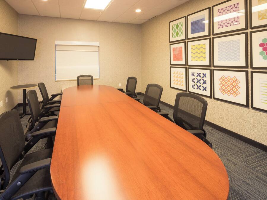 A conference room with a long table, chairs, a projector screen, and framed artwork on the walls.