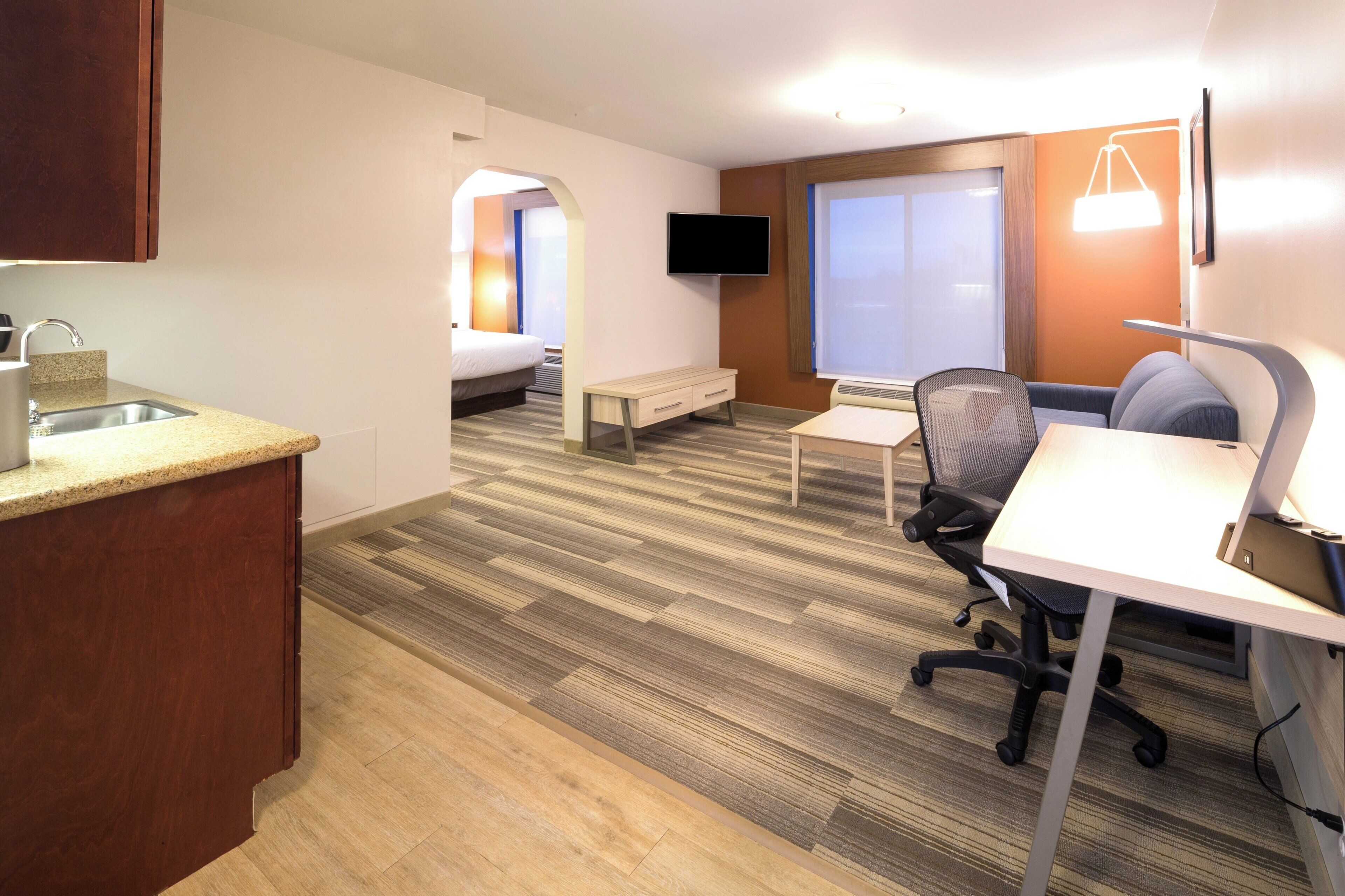 A hotel room with a kitchenette, a bed, a desk, and a chair.