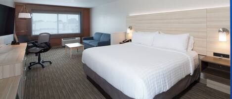 A hotel room with a large bed, a desk with a chair, a small table, a TV, and a window with a view.