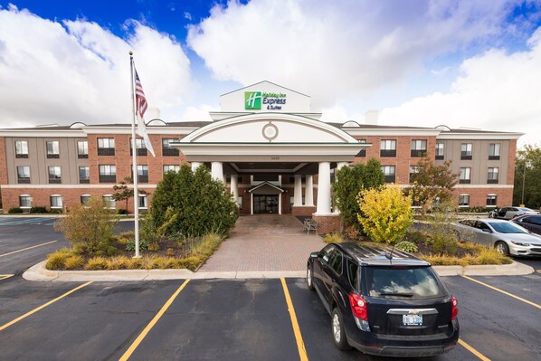 A Holiday Inn Express & Suites building with a brick facade, a central entrance, and a parking lot with a black SUV. - Holiday Inn Express Hotel & Suites Grand Blanc by IHG (Grand Blanc)