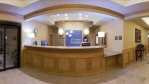 A reception area with a wooden reception desk, a clock, and a sign with a logo. - Holiday Inn Express Hotel & Suites Grand Blanc by IHG (Grand Blanc)