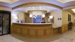 A reception area with a wooden reception desk, a clock, and a sign with a logo. - Holiday Inn Express Hotel & Suites Grand Blanc by IHG (Grand Blanc)