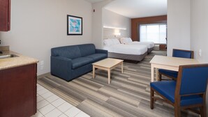 A hotel room with a kitchenette, a sofa, a small table, a bed, and a chair. - Holiday Inn Express Hotel & Suites Grand Blanc by IHG (Grand Blanc)