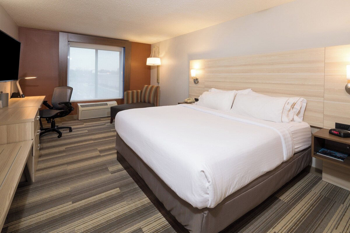 A hotel room with a bed, desk, chair, and a window.