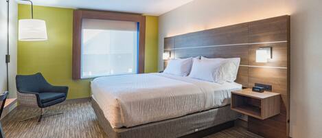 Une chambre d’hôtel moderne avec un grand lit, une table de chevet avec une horloge, une chaise et une fenêtre avec des stores.
