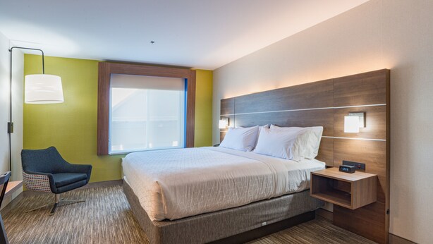Ein modernes Hotelzimmer mit einem großen Bett, einem Schreibtisch mit Lampe und Blick ins Freie.