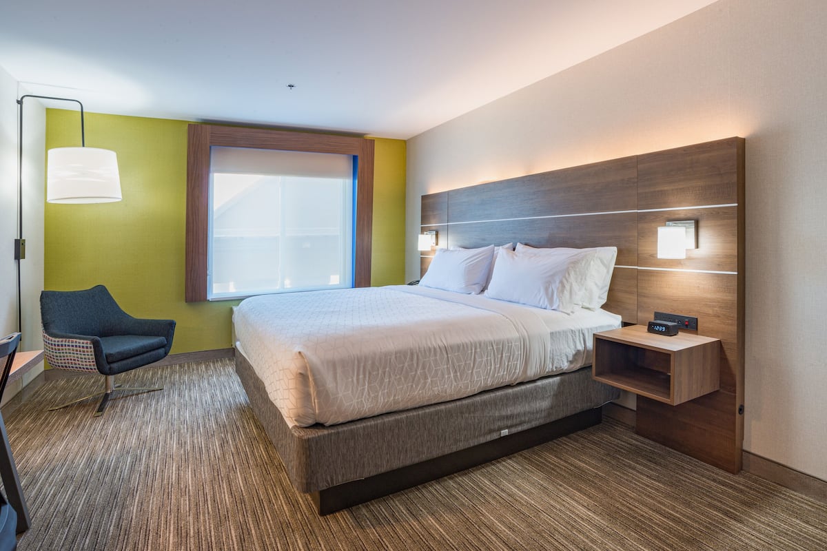 A modern hotel room with a large bed, a desk with a lamp, and a view of the outdoors.