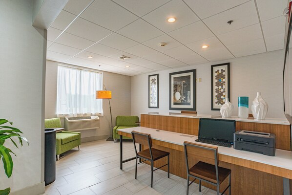 Une chambre d’hôtel équip ée d’un bureau, de chaises, d’un ordinateur, d’une imprimante, d’une lampe, d’une fenêtre avec des rideaux et d’une plante.